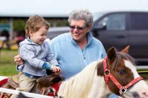 An old woman helps a young boy ride a pony at a country fair.