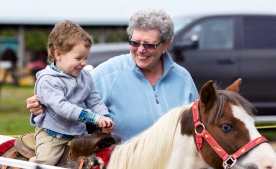 An old woman helps a young boy ride a pony at a country fair.