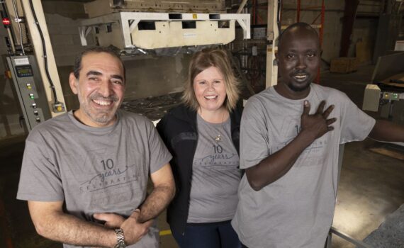 Three workers share a laugh on the factory floor.