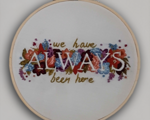 A embroidery hoop with flowers and the words “We Have Always Been Here.”