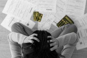 A woman sits cross legged on the floor running her hands through her hair while working on a budget.