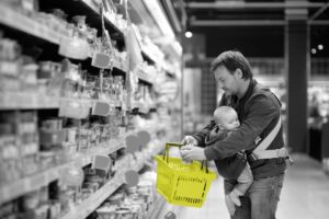 A man grocery shops with a baby in a sling.