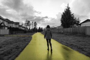 A young woman walks down a wet laneway between rows of single-family homes.