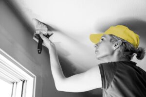 A young woman painting a white ceiling.