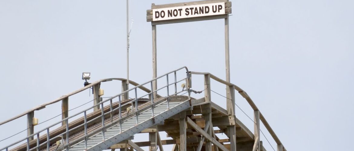 A warning sign reading “do not stand up” at the top of a wooden rollercoaster.