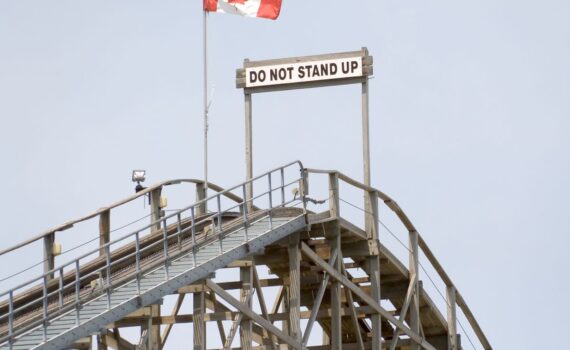 A warning sign reading “do not stand up” at the top of a wooden rollercoaster.